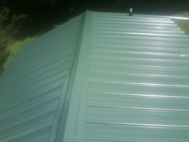 New green metal panels meeting at the ridge of a roof — Flat Roof Repair work by our crew in Windsor